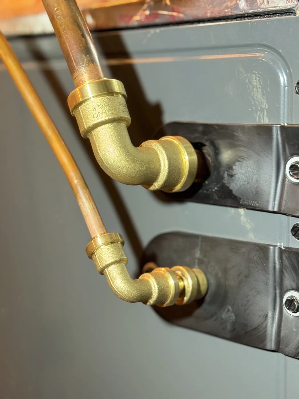Close view of copper refrigerant lines joined to an indoor coil with brass fittings