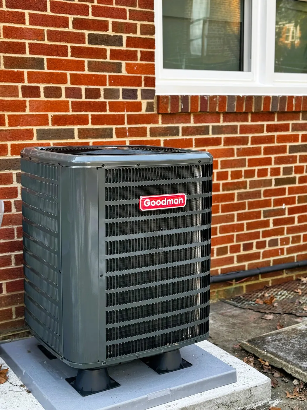 A Goodman condenser on a pad against a red brick wall