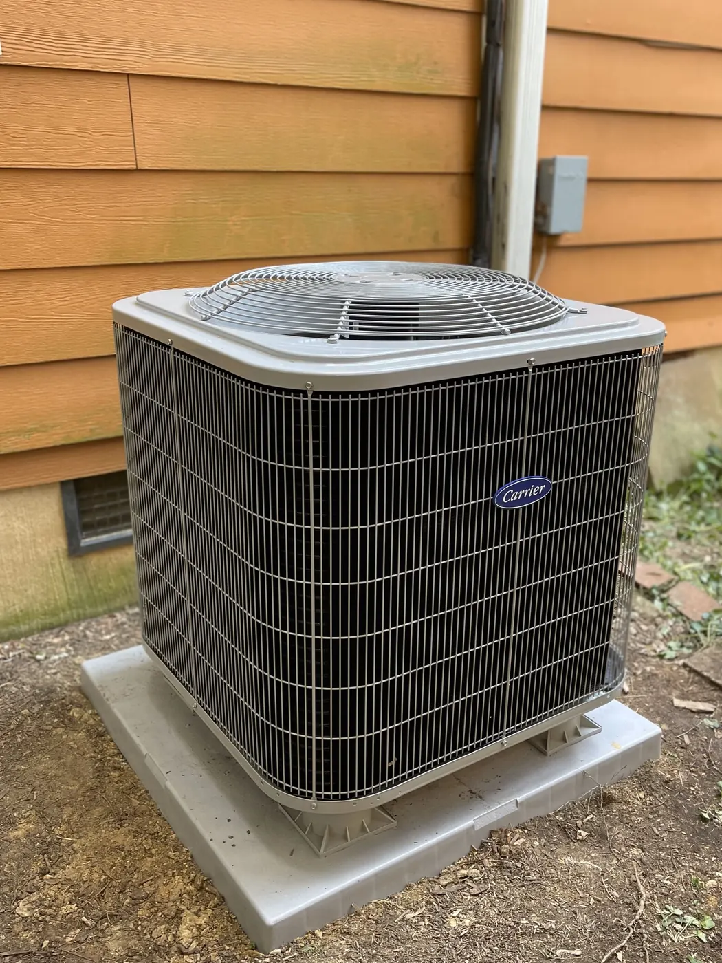 An outdoor AC condenser on a concrete pad beside tan wood siding