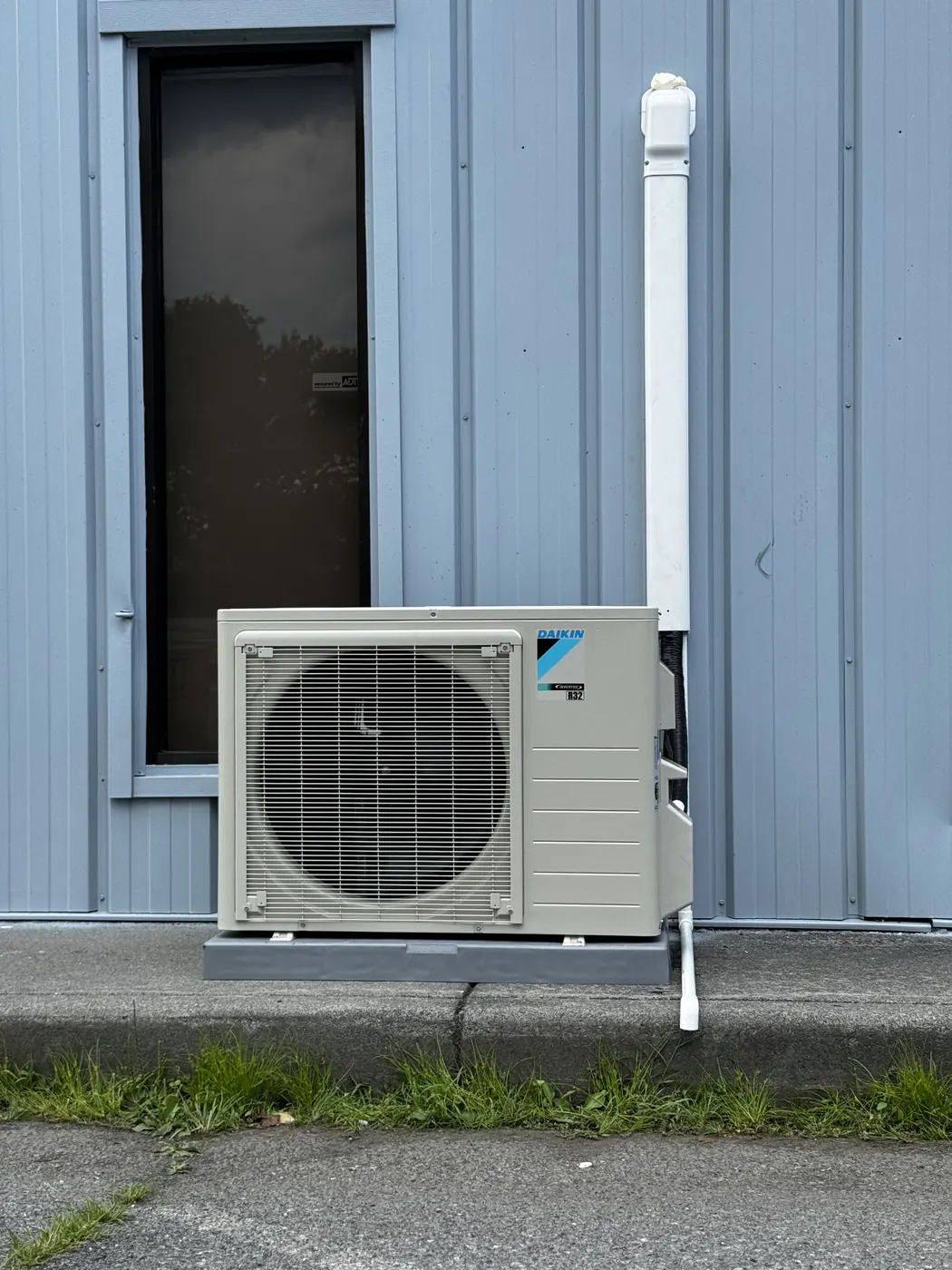 A Daikin ductless outdoor unit mounted on a pad against gray siding with a clean line-set cover
