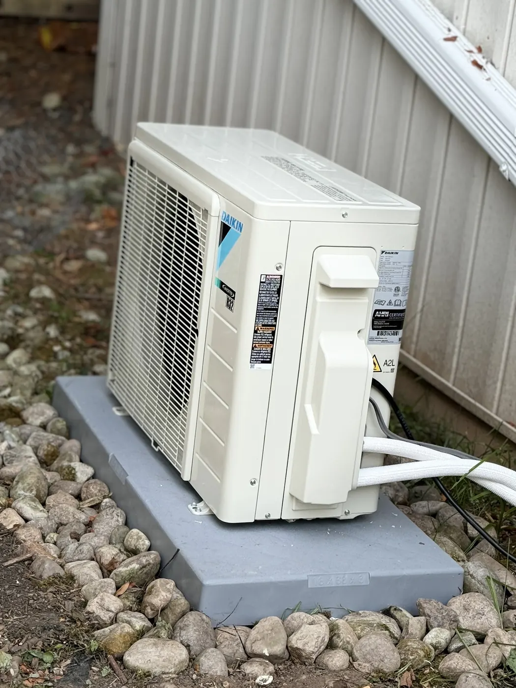 A Daikin ductless outdoor unit on a plastic pad set in river stone beside a house
