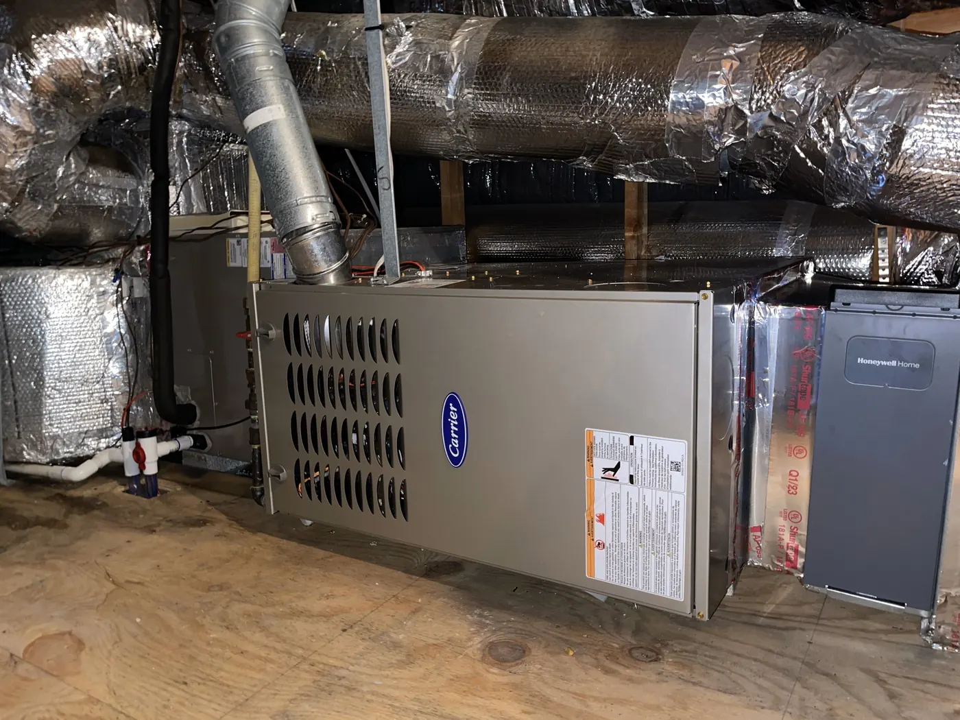 A new Carrier furnace in a basement with fresh insulated ductwork running overhead