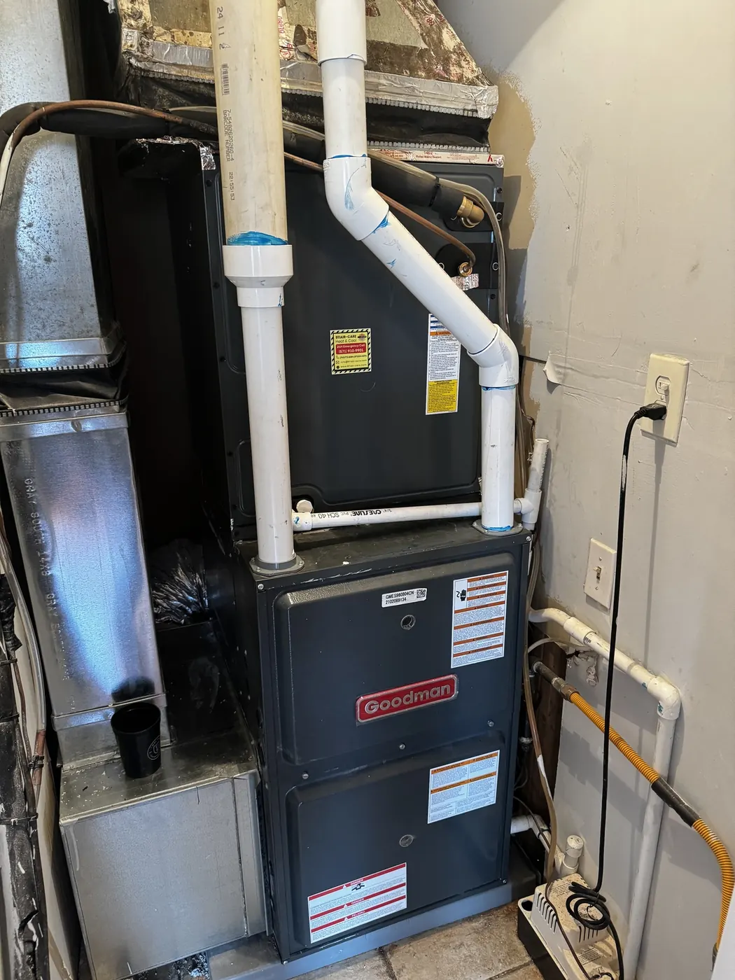 A new Goodman gas furnace and coil installed in a basement with white PVC venting