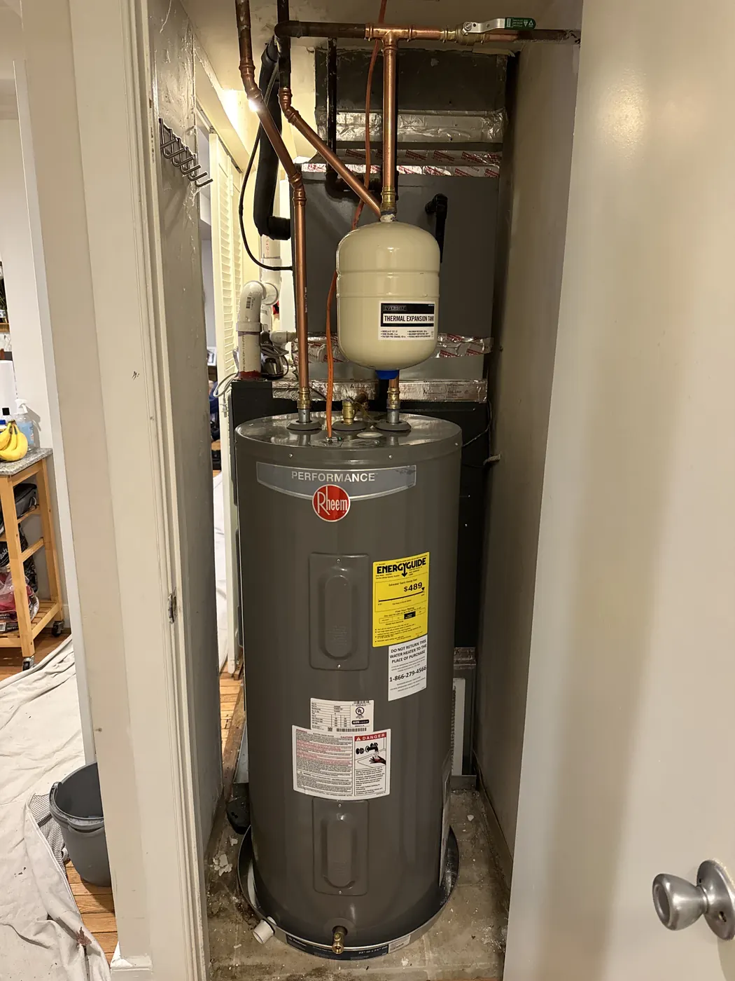 A new Rheem electric water heater with an expansion tank on the copper piping, installed in a closet