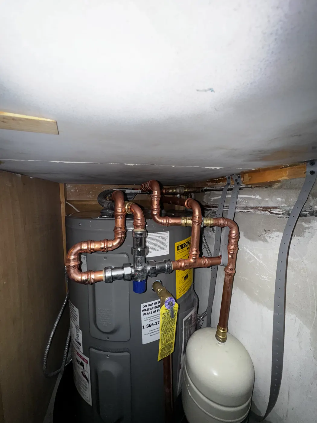 An electric water heater with new copper piping and an expansion tank in a tight closet
